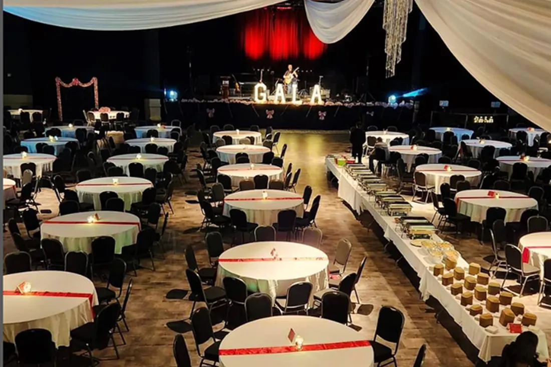 GALA in marquee letters on stage above a banquet hall set with round tables
