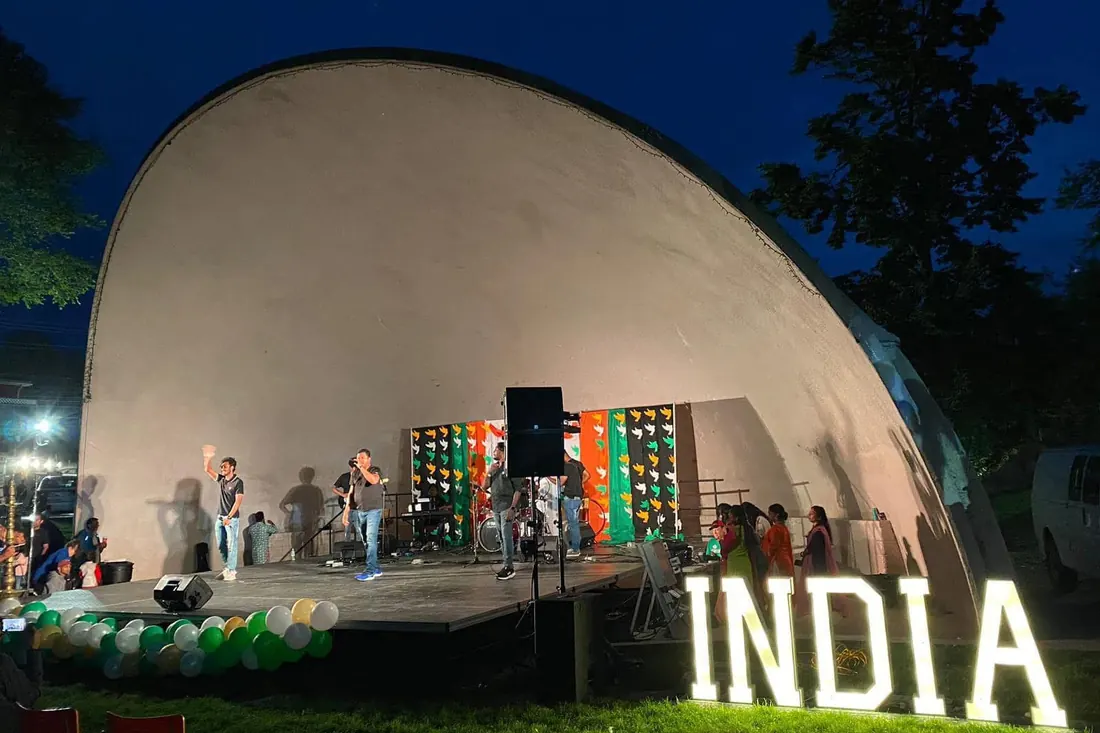 INDIA in lit marquee letters beside an outdoor band shell stage at dusk