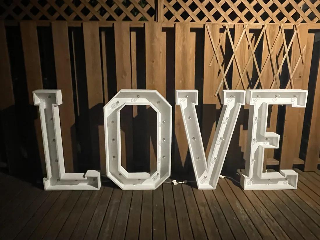 The LOVE letters unlit, showing their white finish against a wooden fence